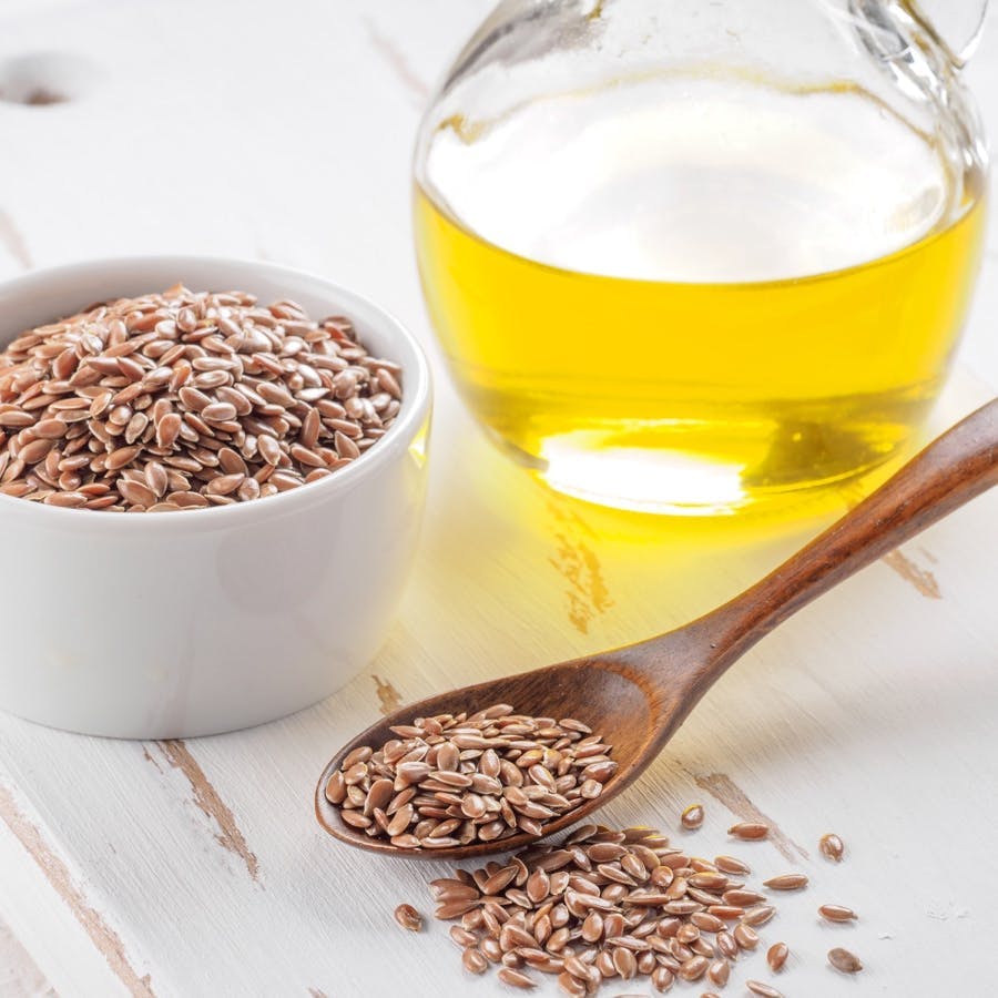 Brown flax seeds in spoon and flaxseed oil in glass bottle on white wooden background. Flax oil is rich in omega-3 fatty acid.
