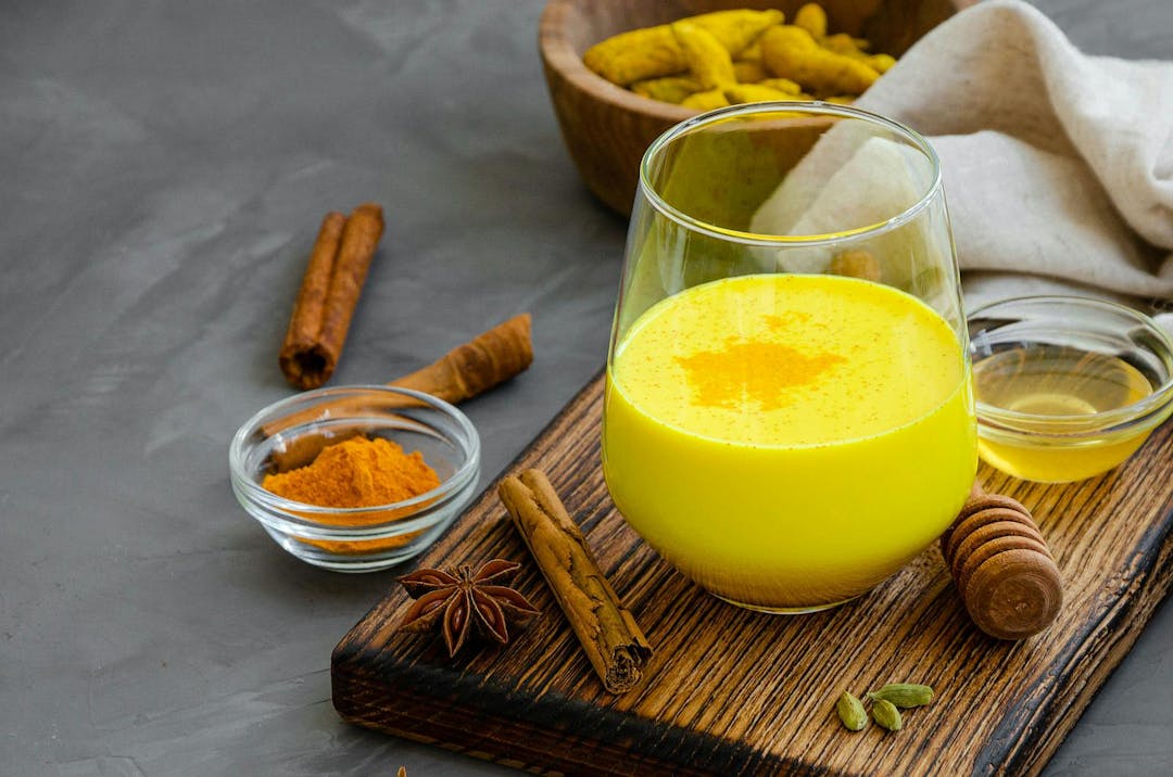 Golden milk in a glass on a wooden board with honey and other spices. A healthy drink made from milk and turmeric. Horizontal orientation. Copy space
