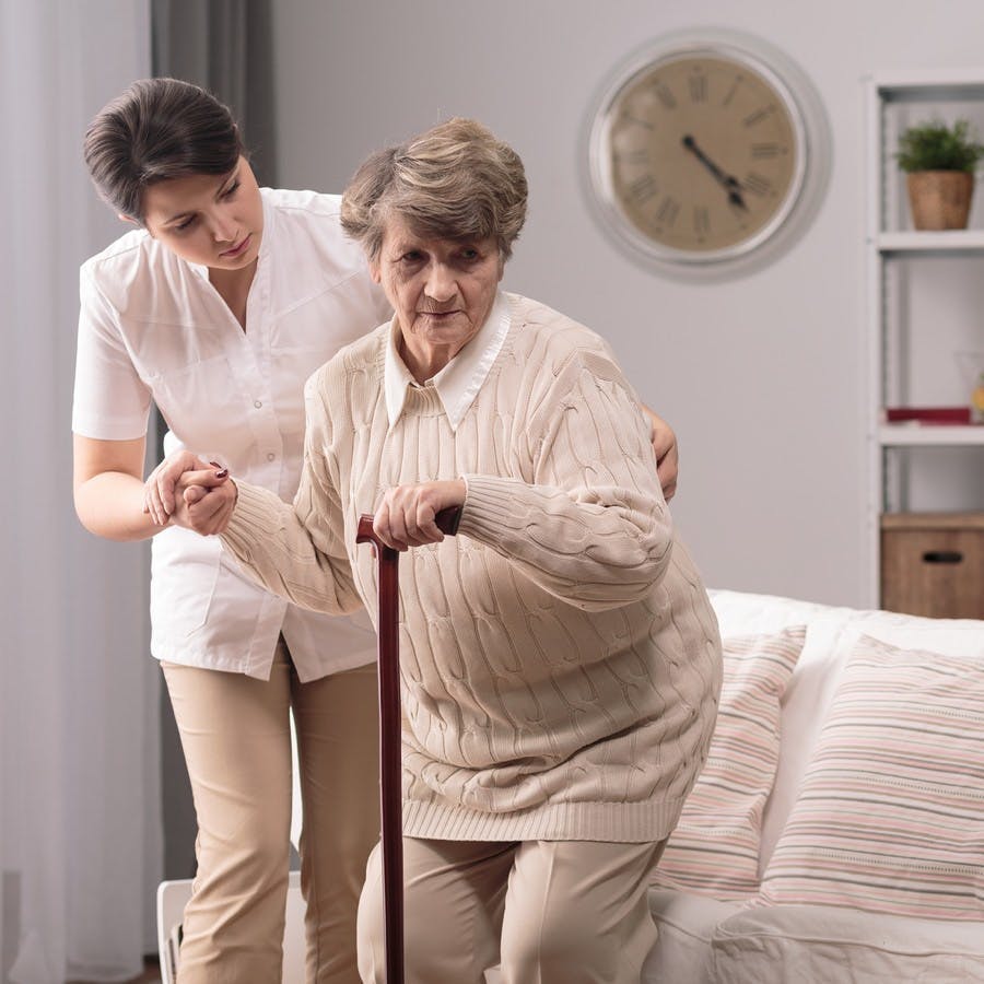 Young caregiver helping older lady to stand up
