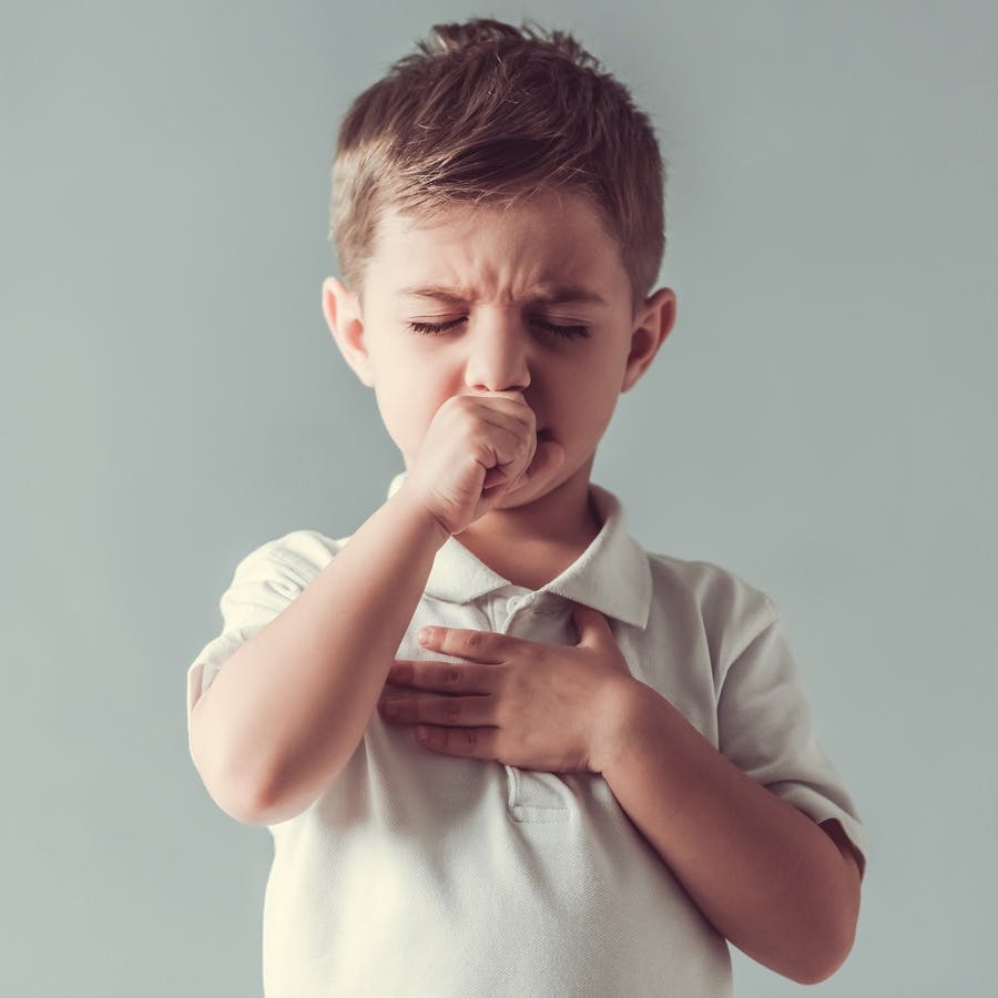 Cute little boy is coughing on gray background
