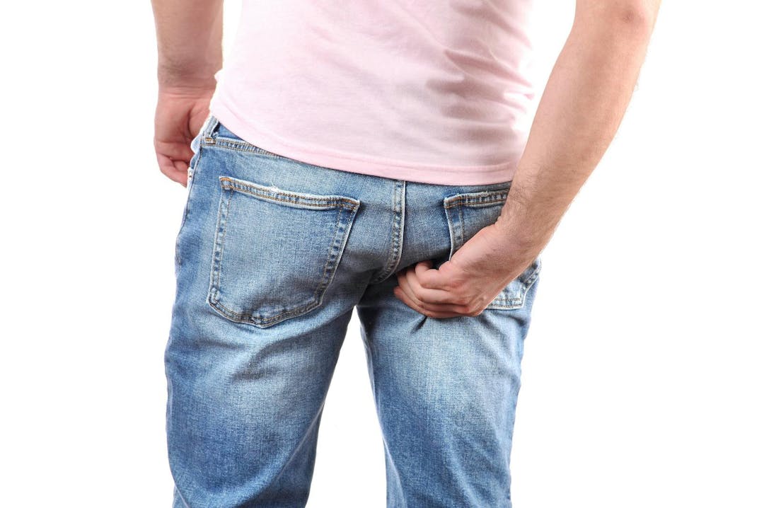 Man in jeans scratching hand his itchy bottom
