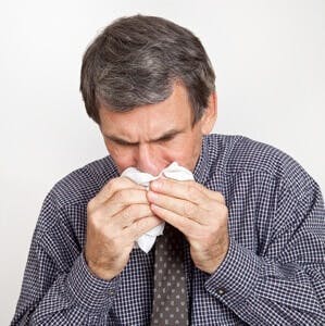 Closeup of mature man sneezing into a handkerchief, suffering with cold or flu.
