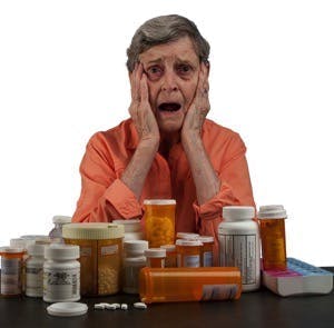 An elderly woman with a tableful of medications looking overwhelmed and confused
