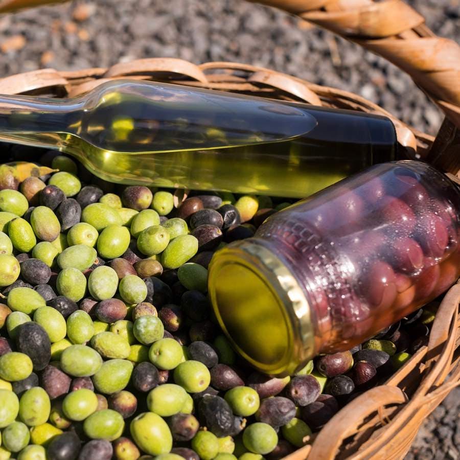 Close-up of olives, jar and olive oil bottle in basket on a sunny day
