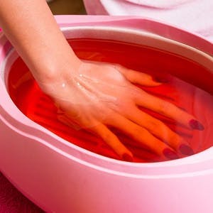 Female hand and orange paraffin wax in bowl. Manicure and skincare. Woman girl in beauty spa salon.

