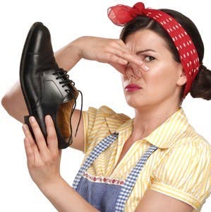 Beautiful vintage housekeeper holding a smelly shoes with facial expression on white
