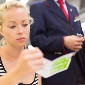 Young woman traveling by train, having her ticket checked by the train conductor
