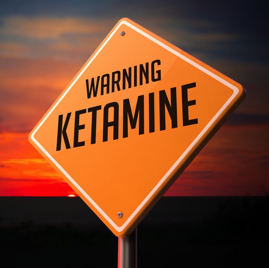 Ketamine on Warning Road Sign on Sunset Sky Background.
