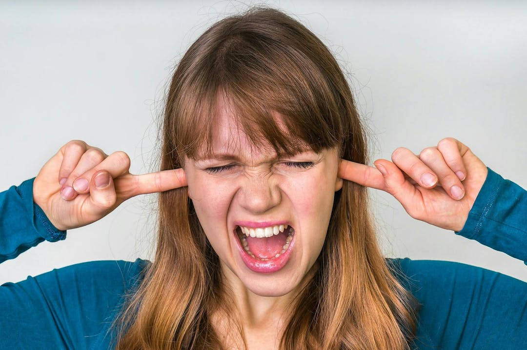 Woman closes ears with fingers to protect from loud noise isolated on white
