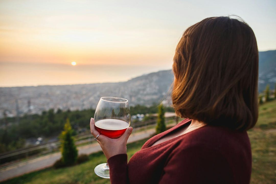 Woman drinking red wine on sunset mountains, close up of hand holding glass of wine. Elegant woman enjoying beautiful mountain and sea landscape on sunset
