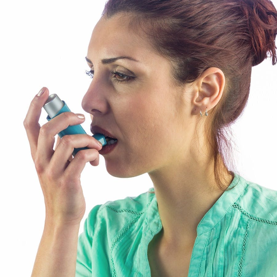 Woman looking away while using asthma inhaler against white background
