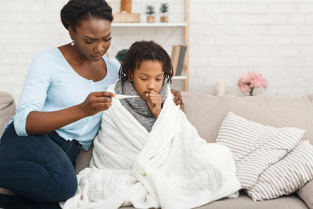 Flu Concept. Worried black mother checking her daughters temperature, child covered in blanket, copy space
