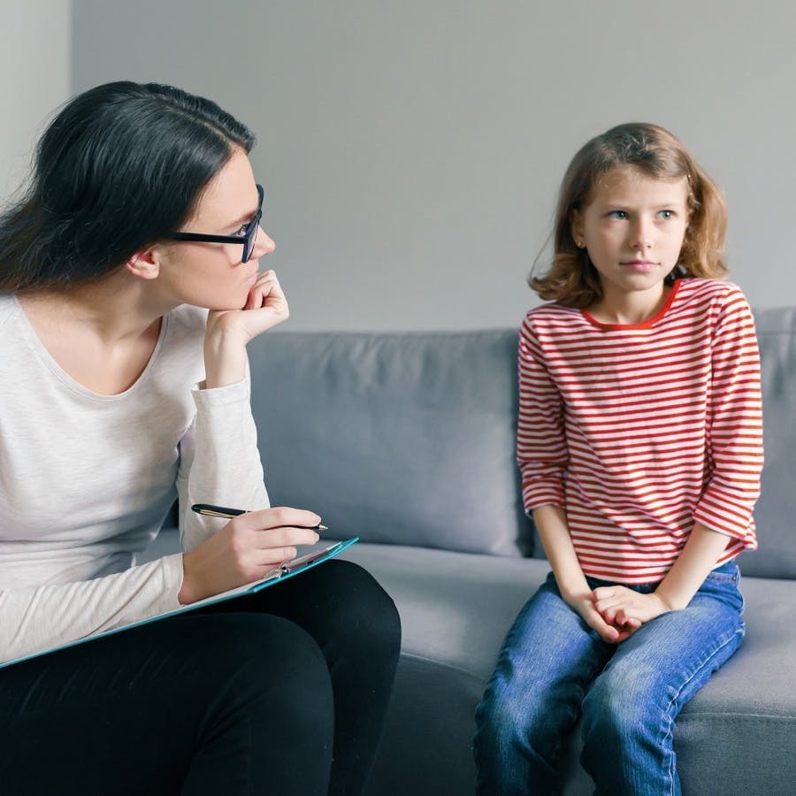 Professional child psychologist talking with child girl in office.
