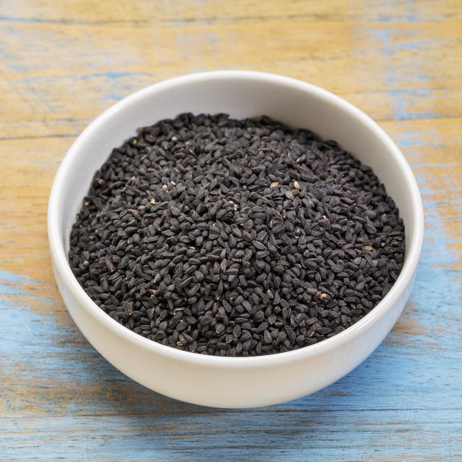 Black cumin seeds (Nigella sativa) in white ceramic bowl against grunge wood
