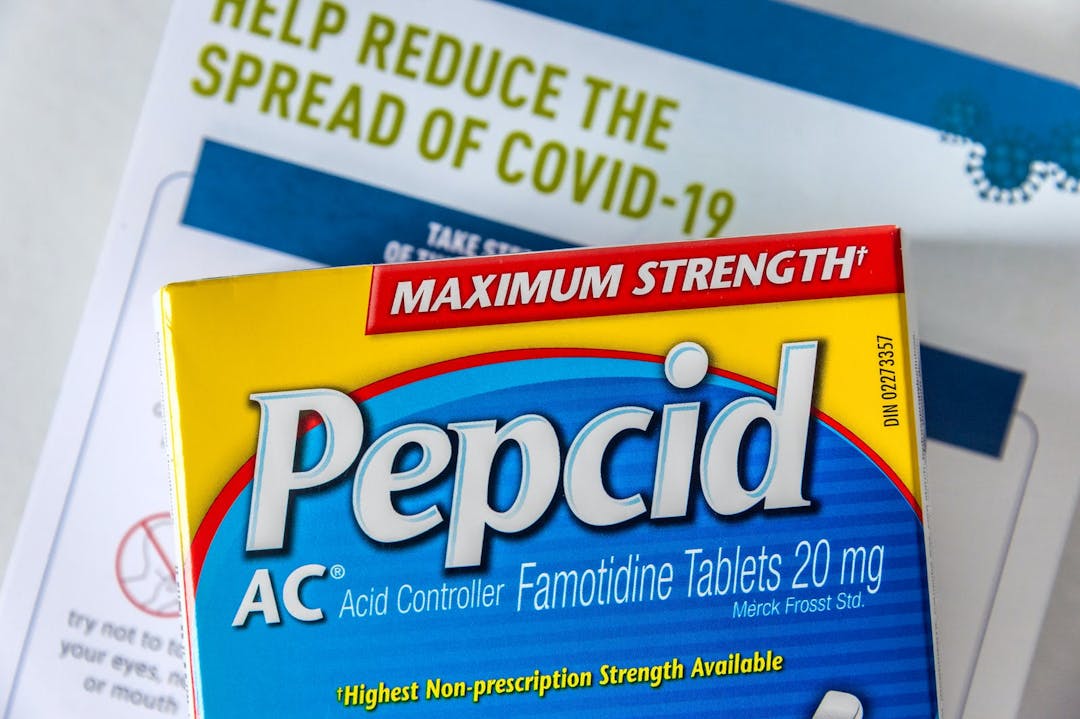 Montreal, CA &#8211; 27 April 2020: Box of Pepcid AC antacid medicine in front of a Covid-19 prevention document
