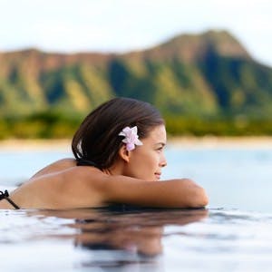 Infinity pool resort woman relaxing at sunset overlooking Waikiki beach in Honolulu city, Oahu island, Hawaii, USA. Wellness and relaxation concept for summer vacations.
