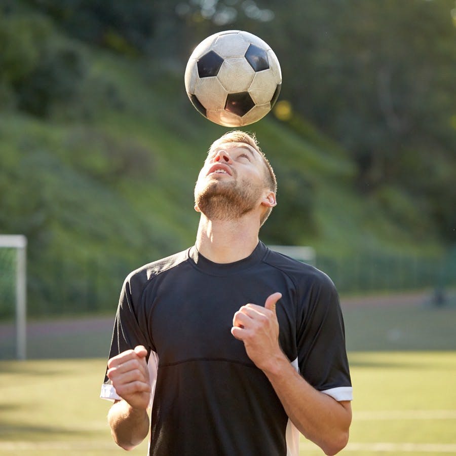 Sport, football and people &#8211; soccer player playing and juggling ball using header technique on field
