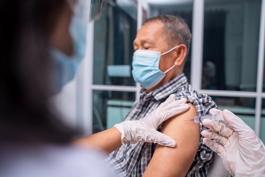 Doctor making a vaccination in the shoulder of old patient, Flu Vaccination Injection on Arm, coronavirus, covid-19 vaccine disease preparing for human clinical trials vaccination shot.
