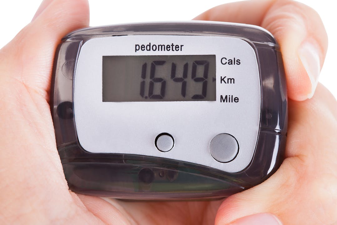 Close-up Of Hand Holding Digital Pedometer On White Background

