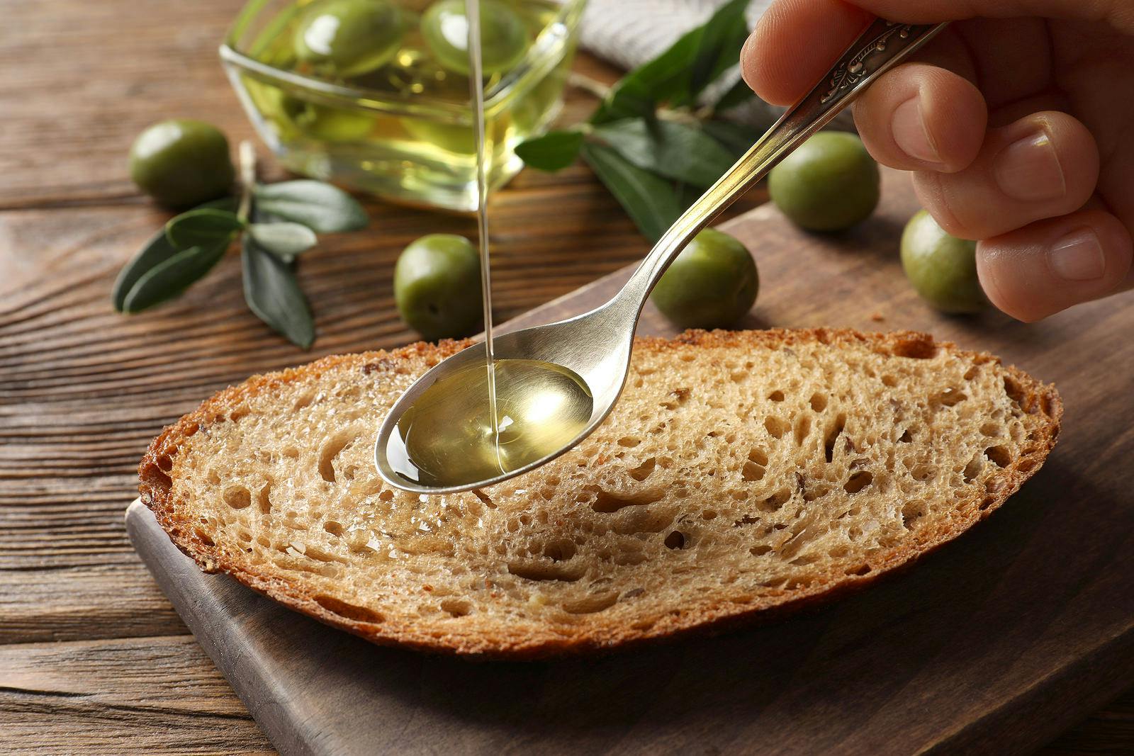 pouring olive oil onto spoon over a slice of bread