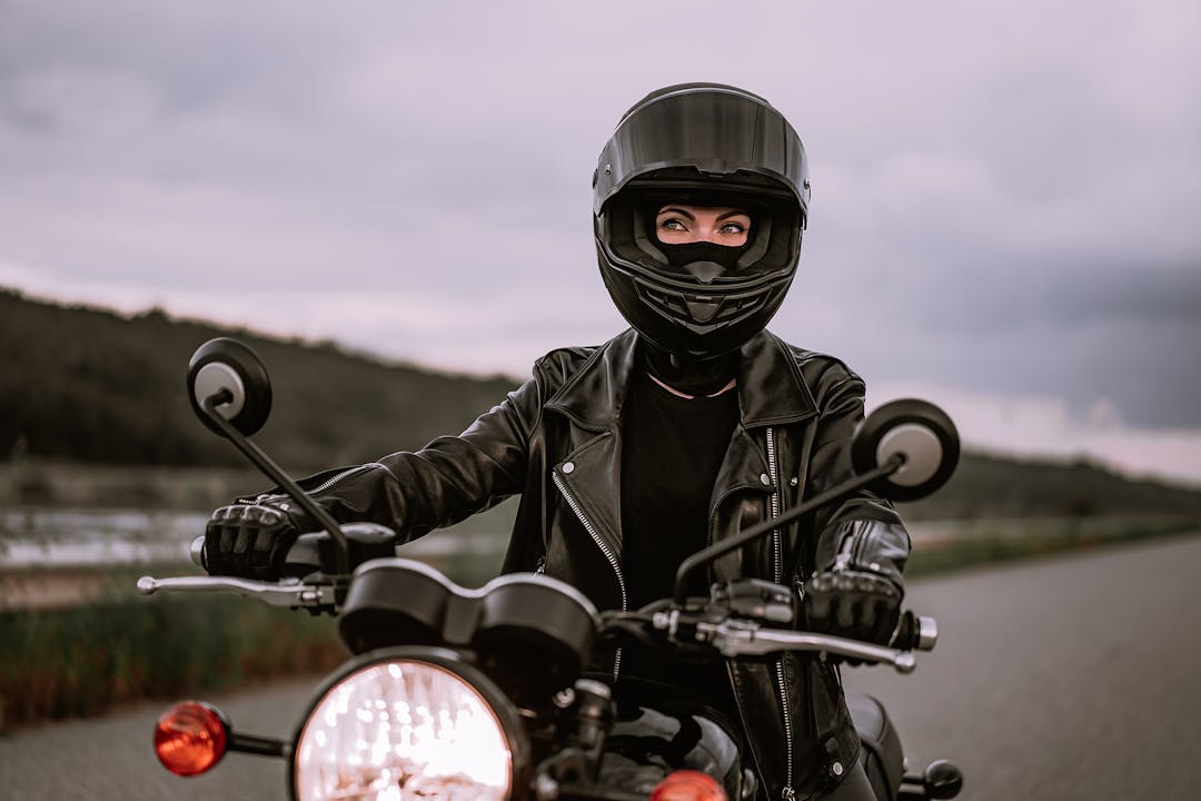 Portrait of confident motorcyclist woman in motorcycle helmet. Young driver biker looking away outdoors alone on highway. Ready for trip. Cafe racers, motorbike aesthetics and vintage design concept.
