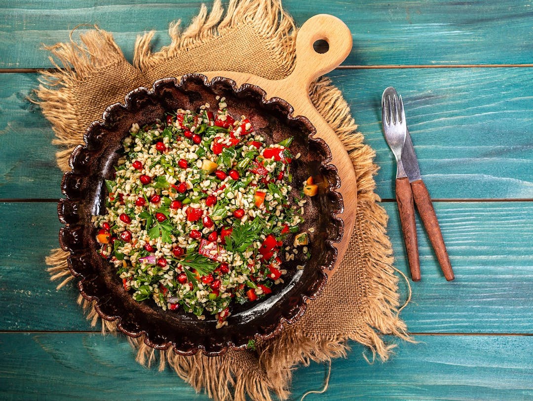 A bowl of delicious fresh tabouli with parsley, mint, tomato, onion, olive oil, lemon juice, and bulgar wheat. Traditional oriental salad Tabouleh.

